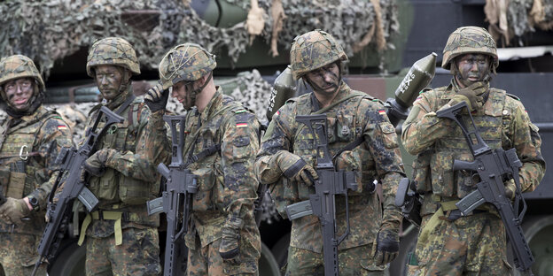 Mehrere Soldaten in Uniform mit geschwärzten Gesichtern und Gewehren