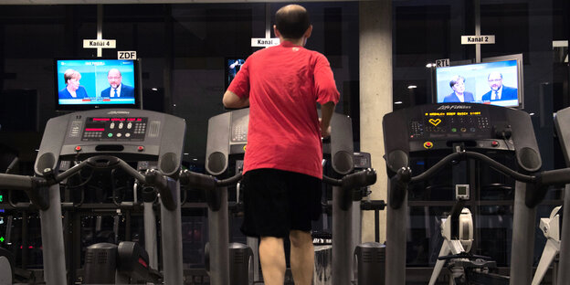 Ein Mann läuft auf einem Laufband und sieht im Fernsehen des Duell zwischen Angela Merkel und Martin Schulz