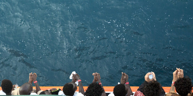Menschen stehen an der Reling eines Schiffes und blicken auf das Meer