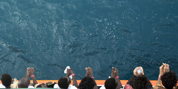 Menschen stehen an der Reling eines Schiffes und blicken auf das Meer Menschen stehen an der Reling eines Schiffes und blicken auf das Meer