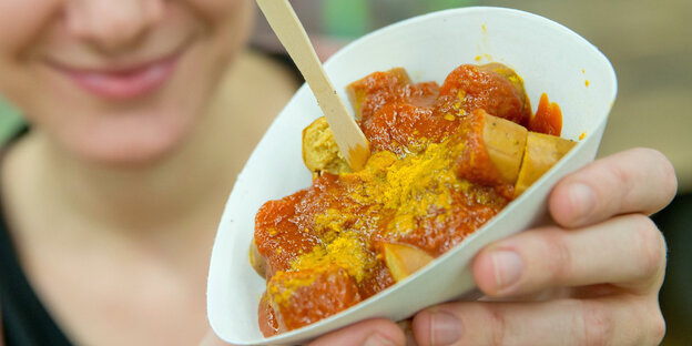 Jemand hält lächelnd eine Papiertüte, in der Curry-Wurst liegt, in den Händen Jemand hält lächelnd eine Papiertüte, in der Curry-Wurst liegt, in den Händen