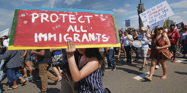 Protestierende, im Vordergrund ein Schild mit der Aufschrift „Protect All Immigrants“ Protestierende, im Vordergrund ein Schild mit der Aufschrift „Protect All Immigrants“