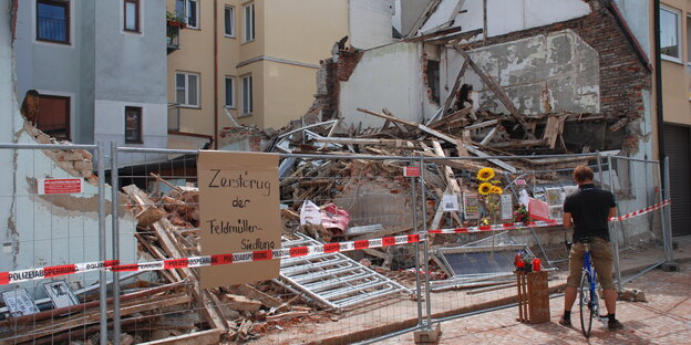 Ein Fahrradfahrer steht vor einem abgerissenen Haus