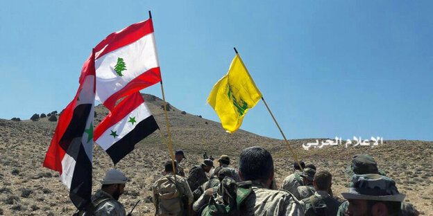 Fahnen der Hisbollah, Libanons und Syriens vor einer kargen Wüstenlandschaft Fahnen der Hisbollah, Libanons und Syriens vor einer kargen Wüstenlandschaft