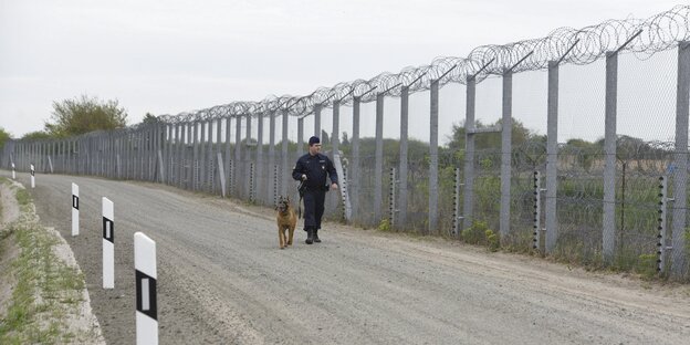 Wachmann mit Hund an einem Grenzzaun Wachmann mit Hund an einem Grenzzaun