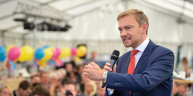 Ein Mann steht vor anderen Menschen und spricht in ein Mikrofon Ein Mann steht vor anderen Menschen und spricht in ein Mikrofon