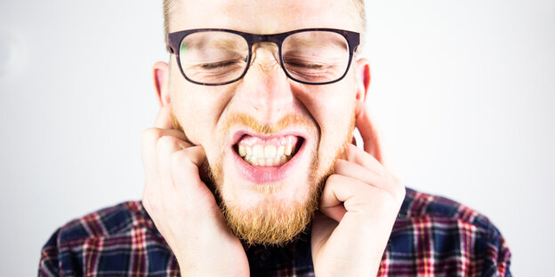 Ein Mann hält sich die Ohren zu und verzieht das Gesicht. Ein Mann hält sich die Ohren zu und verzieht das Gesicht.