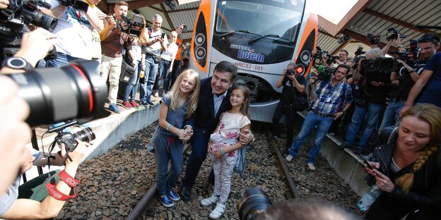 Ein Mann und zwei Mädchen posieren für Fotos vor einem Zug Ein Mann und zwei Mädchen posieren für Fotos vor einem Zug