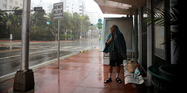 Ein Mann an einer überdachten Bushaltesgtelle, um ihn herum tobt der Hurrican Irma durch die Straßen Ein Mann an einer überdachten Bushaltesgtelle, um ihn herum tobt der Hurrican Irma durch die Straßen