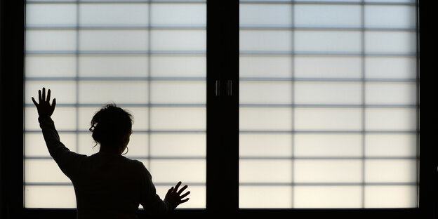 Eine Mensch steht vor einem vergitterten Fenster (Rückansicht) Eine Mensch steht vor einem vergitterten Fenster (Rückansicht)