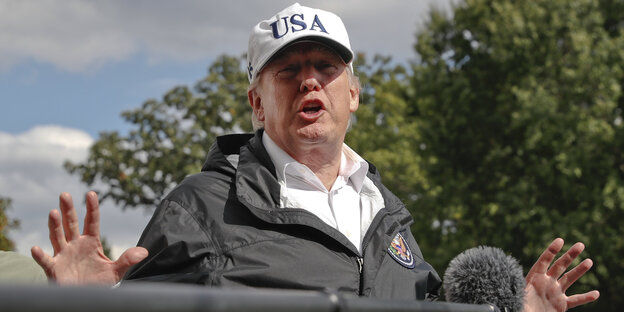 Donald Trump spricht in ein Mikrofon und hebt die Hände Donald Trump spricht in ein Mikrofon und hebt die Hände