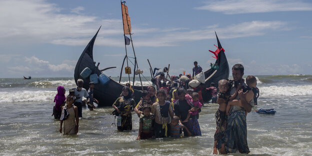 Menschen steigen aus einem Boot aus und waten durchs Wasser