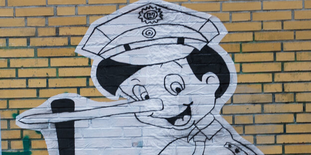 Das weiße Bild von Pinocchio, einer Holzpuppe mit sehr langer Nase, auf einer gelben Hauswand Das weiße Bild von Pinocchio, einer Holzpuppe mit sehr langer Nase, auf einer gelben Hauswand