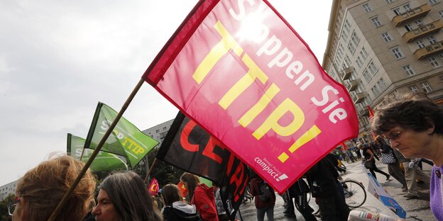 DemonstrantInnen laufen durch eine Stadt und halten eine Fahne hoch auf der steht: "Stoppen Sie TTIP!" DemonstrantInnen laufen durch eine Stadt und halten eine Fahne hoch auf der steht: "Stoppen Sie TTIP!"