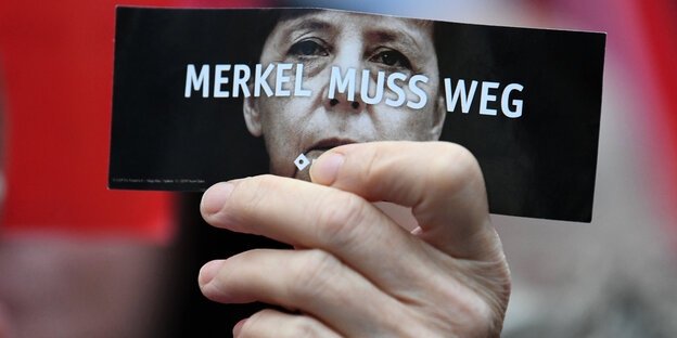 Eine Hand hält einen Flyer mit dem Gesicht von Angela Merkel und dem Spruch "Merkel muss weg" Eine Hand hält einen Flyer mit dem Gesicht von Angela Merkel und dem Spruch "Merkel muss weg"