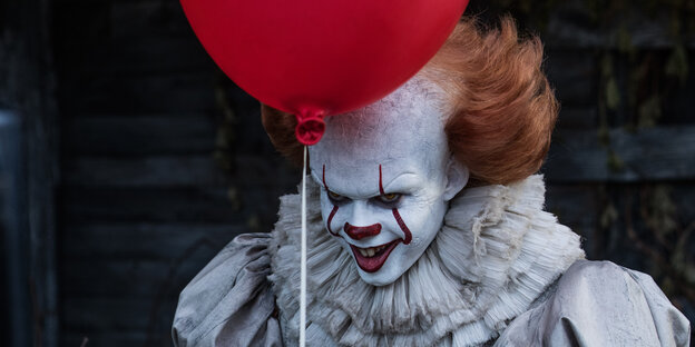 Ein Clown lacht böse. Vor seiner Stirn ist ein Luftballon Ein Clown lacht böse. Vor seiner Stirn ist ein Luftballon