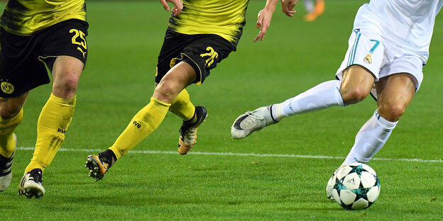 Blick auf die Beine bei einem Fußballspiel. Drei Personen versuchen den Ball zu kriegen Blick auf die Beine bei einem Fußballspiel. Drei Personen versuchen den Ball zu kriegen