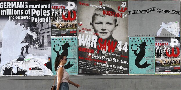 Eine Frau geht an einer Wand mit Plakaten vorbei Eine Frau geht an einer Wand mit Plakaten vorbei