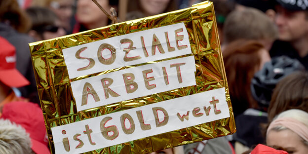Auf einer Demonstration wird ein goldenes Schild mit der Aufschrift "Sozial Arbeit ist Gold wert" hochgehalten. Auf einer Demonstration wird ein goldenes Schild mit der Aufschrift "Sozial Arbeit ist Gold wert" hochgehalten.