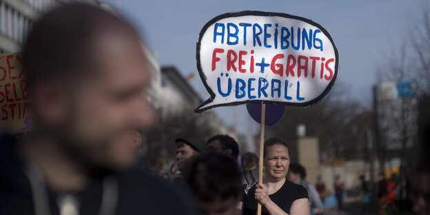 Eine Frau hält auf eine Demo ein Schild hoch, auf dem steht: Abtreibung Frei und Gratis überall