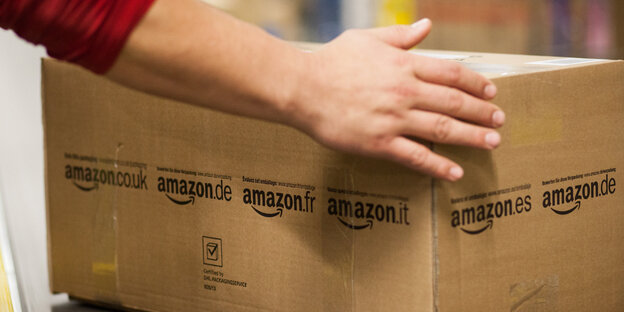 Hände greifen eine Pappbox, auf der Amazon steht Hände greifen eine Pappbox, auf der Amazon steht