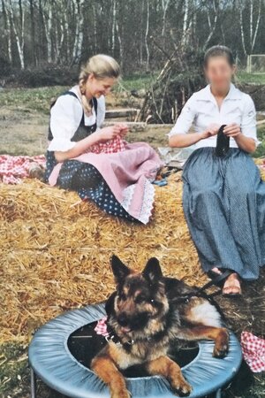 Heidi Benneckenstein sitzt als Jugendliche auf einem Strohballen und näht, vor ihr liegt ein Schäferhund Heidi Benneckenstein sitzt als Jugendliche auf einem Strohballen und näht, vor ihr liegt ein Schäferhund