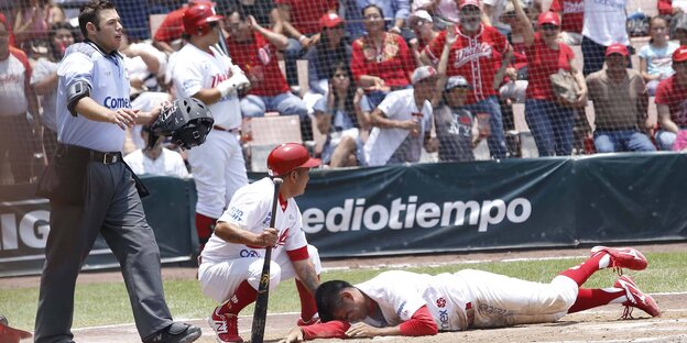 Zwei Baseball-Spieler auf dem Spielfeld, einer liegt auf dem Boden, der andere hockt neben ihm. Zwei Baseball-Spieler auf dem Spielfeld, einer liegt auf dem Boden, der andere hockt neben ihm.