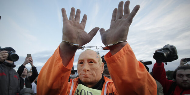 Ein Mann mit einer Putin-Maske hebt beide Hände die mit Handschellen verbunden sind Ein Mann mit einer Putin-Maske hebt beide Hände die mit Handschellen verbunden sind