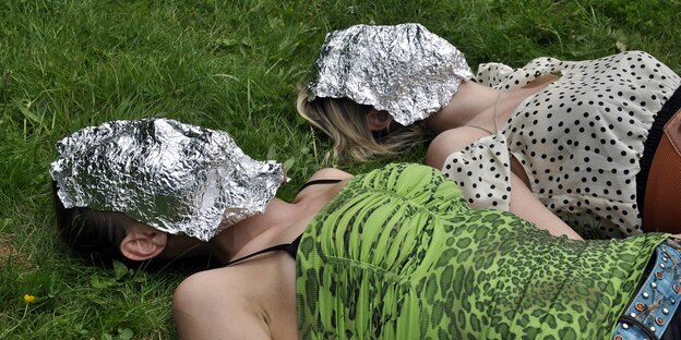 Zwei Frauen liegen auf einer Wiese, sie haben Masken aus Alufolie im Gesicht Zwei Frauen liegen auf einer Wiese, sie haben Masken aus Alufolie im Gesicht
