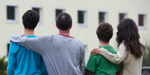Rückansicht einer syrischen Familie, die vor einem Asylwohnheim sitzt Rückansicht einer syrischen Familie, die vor einem Asylwohnheim sitzt