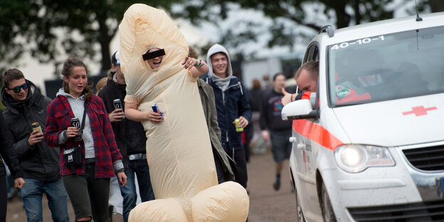 Ein Mann läuft als Penis verkleidet und mit Bier in der Hand auf der Straße.