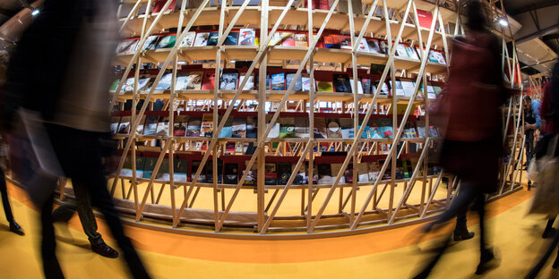 hohes Regal mit vielen Büchern, an dem schemenhaft Menschen vorbeigehen hohes Regal mit vielen Büchern, an dem schemenhaft Menschen vorbeigehen