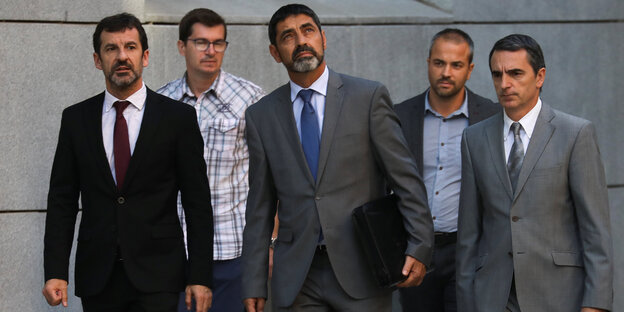 Fünf Männer gehen vor einem grauen Gebäude Fünf Männer gehen vor einem grauen Gebäude