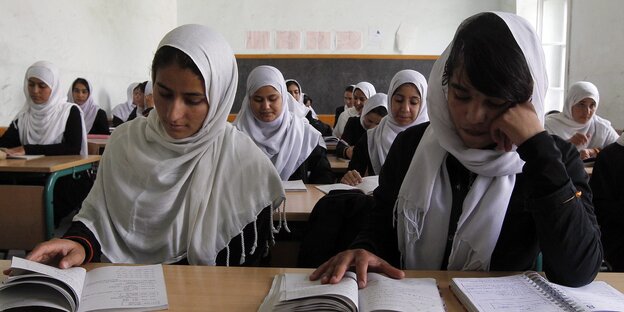 Mädchen mit aufgeschlagenen Büchern in einem Klassenzimmer Mädchen mit aufgeschlagenen Büchern in einem Klassenzimmer