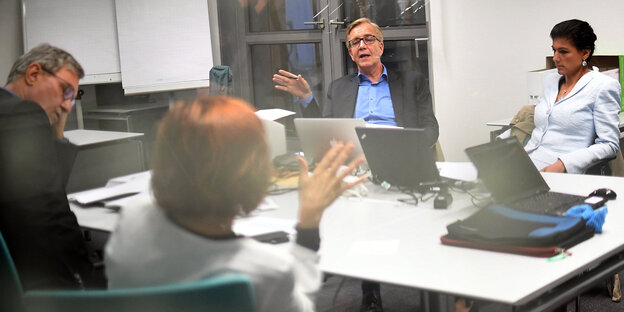 Vier Personen diskutieren an einem Tisch hinter einer Glasscheibe Vier Personen diskutieren an einem Tisch hinter einer Glasscheibe