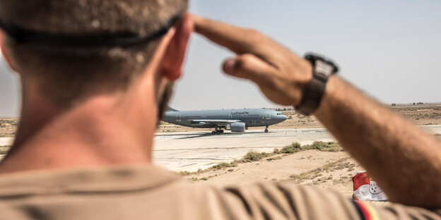 Ein Soldat salutiert, dahintere ein Flugzeug Ein Soldat salutiert, dahintere ein Flugzeug