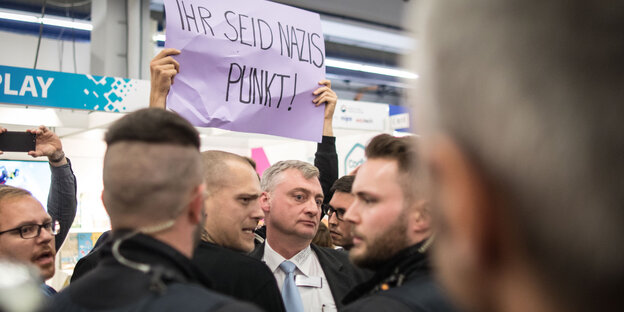 In einer Menschenmenge wird ein Schild hochgehalten, auf dem steht "Ihr seid Nazis, Punkt!" In einer Menschenmenge wird ein Schild hochgehalten, auf dem steht "Ihr seid Nazis, Punkt!"