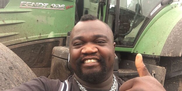 Ein Mann steht vor einem Traktor und hält den Daumen hoch Ein Mann steht vor einem Traktor und hält den Daumen hoch