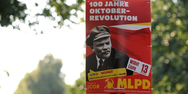 Ein Mann mit altmodischer Arbeitsmütze blickt von einem roten Plakat Ein Mann mit altmodischer Arbeitsmütze blickt von einem roten Plakat