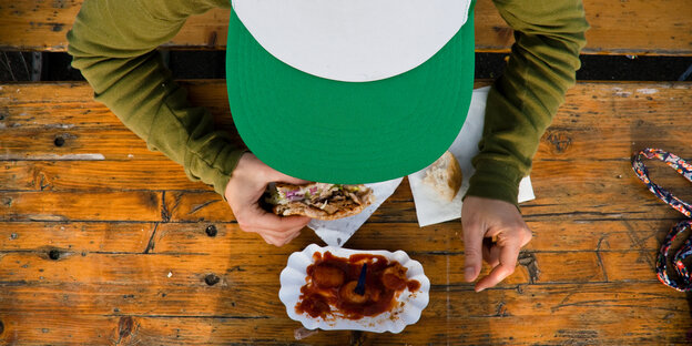 Eine Person mit Basecap isst Currywurst Eine Person mit Basecap isst Currywurst
