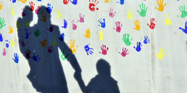 Der Schatten eines Mannes mit zwei Kindern auf einer Wand mit farbigen Handabdrücken Der Schatten eines Mannes mit zwei Kindern auf einer Wand mit farbigen Handabdrücken