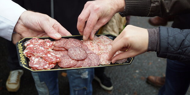 Hände, die zu Wurstscheiben greifen Hände, die zu Wurstscheiben greifen