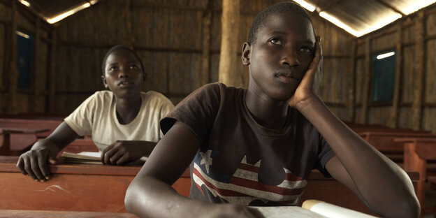 Zwei sudanesische Mädchen sitzen hintereinander an Schultischen Zwei sudanesische Mädchen sitzen hintereinander an Schultischen