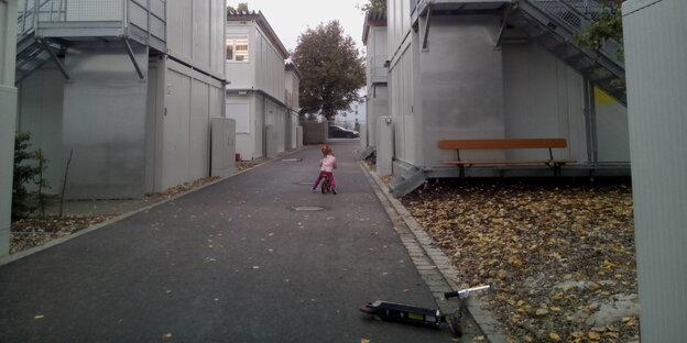 Ein kleines Mädchen fährt mit einem Fahrrad zwischen Containern einen Weg entlang Ein kleines Mädchen fährt mit einem Fahrrad zwischen Containern einen Weg entlang