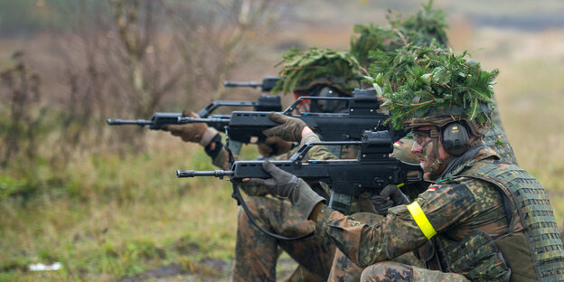 Mehrere Soldaten knien in einer Reihe mit angelegtem Gewehr und Tarnhüten. Mehrere Soldaten knien in einer Reihe mit angelegtem Gewehr und Tarnhüten.