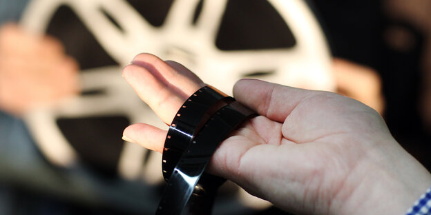 Hand mit Filmstreifen vor Filmrolle. Hand mit Filmstreifen vor Filmrolle.