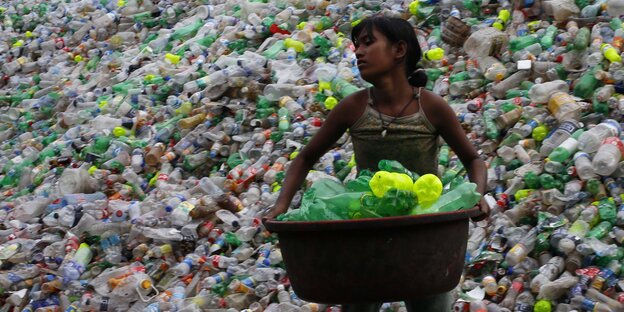 Mädchen trägt Korb voller Plastikflaschen, dahinter ein riesiger Haufen Flaschen Mädchen trägt Korb voller Plastikflaschen, dahinter ein riesiger Haufen Flaschen