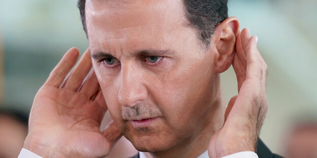 Assad hält sich die Hände hinter die Ohren und guckt betreten Assad hält sich die Hände hinter die Ohren und guckt betreten