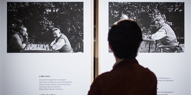 Eine Person sieht sich in der Ausstellung ein Bild an, auf dem Brecht und Benjamin Schach spielem Eine Person sieht sich in der Ausstellung ein Bild an, auf dem Brecht und Benjamin Schach spielem