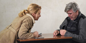 Tatort-Kommissarin Maria Furtwängler lehnt sich über einen Tisch, rechts sitzt ein weinender Mann